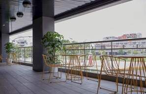 Área externa com assentos de metal e uma planta em vaso, com vista para a cidade.