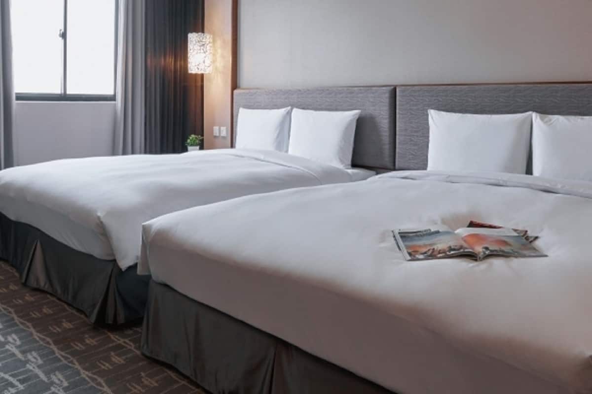 Een hotelkamer met twee bedden, een nachtkastje, een lamp en een raam met gordijnen.