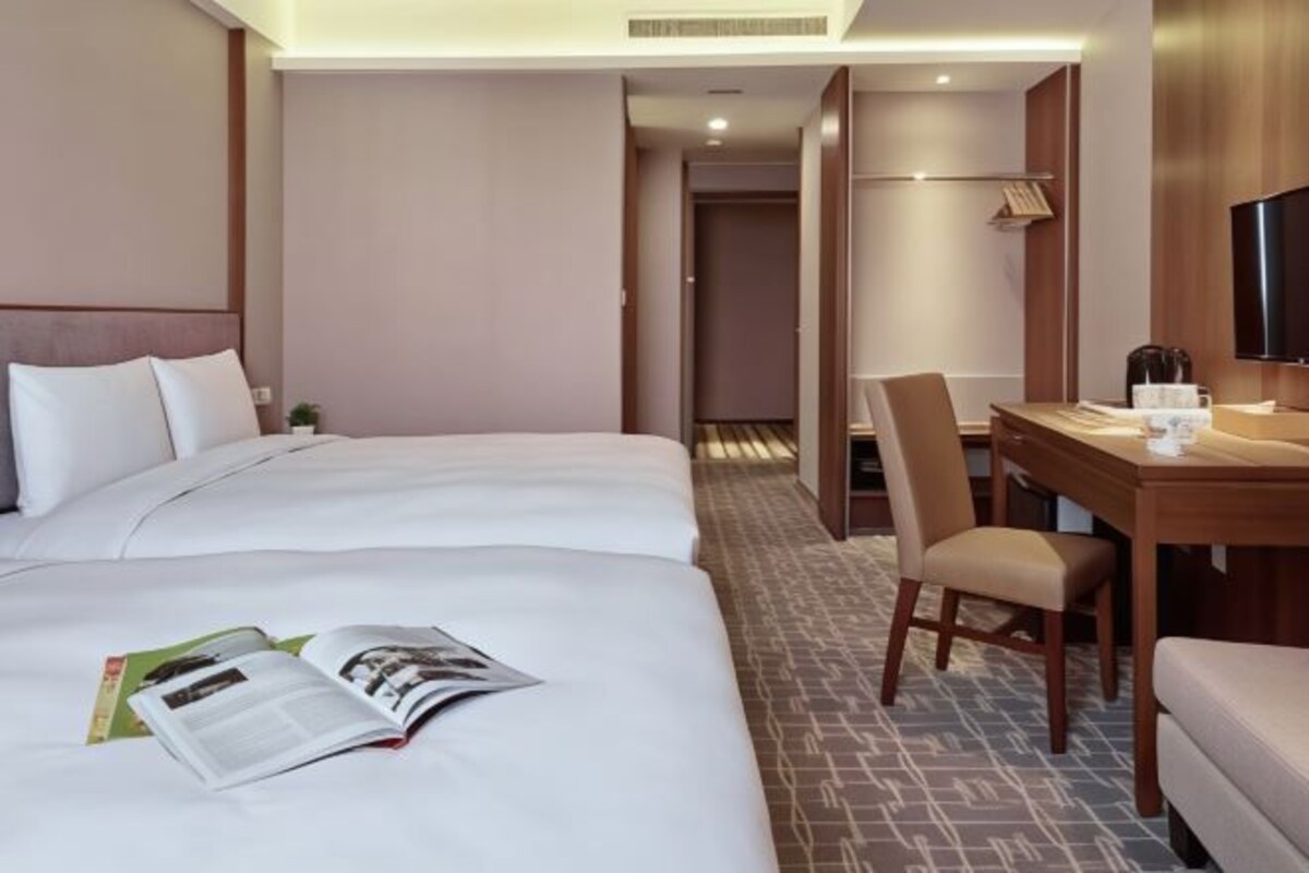 Habitación de hotel con dos camas, un escritorio con silla, una televisión y una estantería.