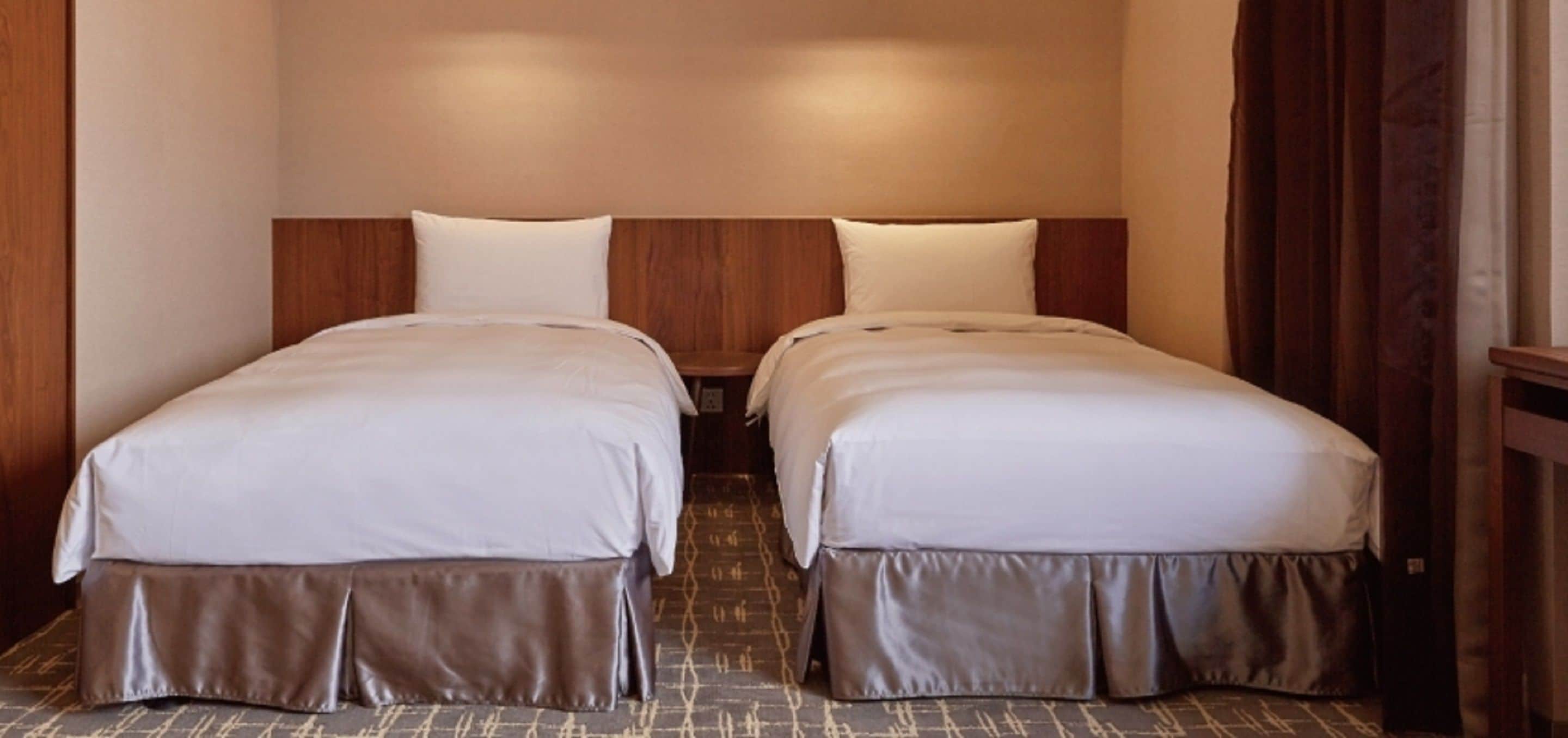 Habitación de hotel con dos camas individuales, cada una con cabecero de madera y ropa de cama blanca.