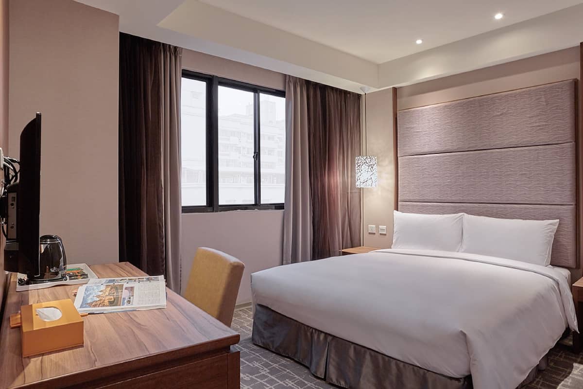 Een hotelkamer met een groot bed, een bureau met stoel, een televisie en een raam met gordijnen.