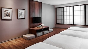A hotel room with a large window, a TV mounted on the wall, and two beds.