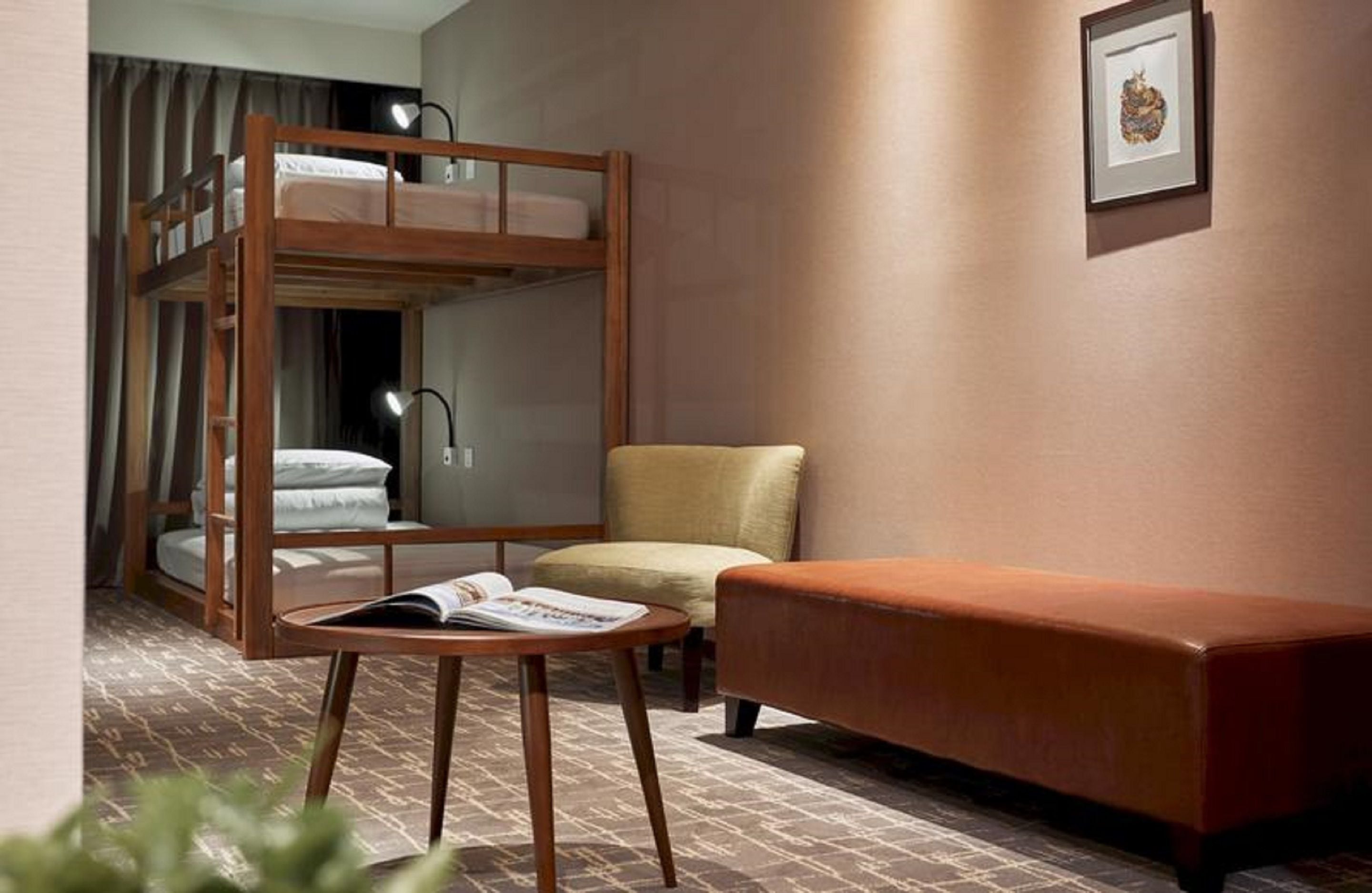 Une pièce avec un lit superposé, une petite table avec un livre, une chaise et un canapé.