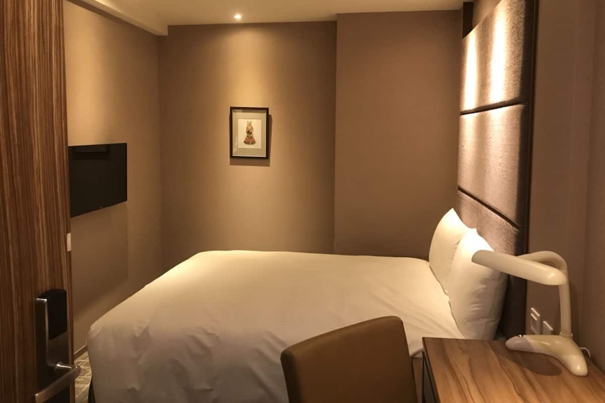 Een hotelkamer met een groot bed, nachtkastje, stoel, een tv aan de muur en een ingelijst kunstwerk.