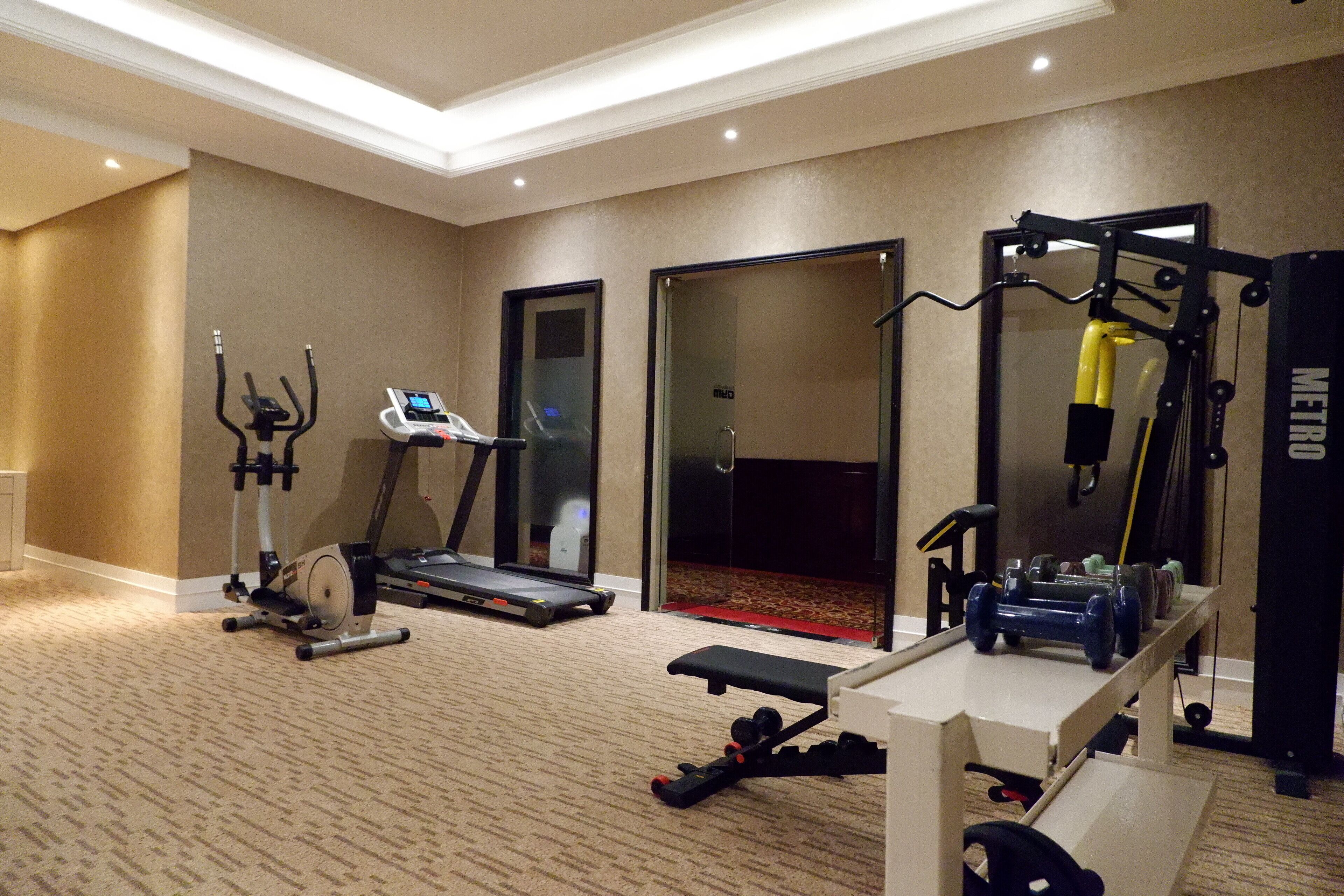 A hotel fitness room with a treadmill, elliptical, bench press, and weight bench.
