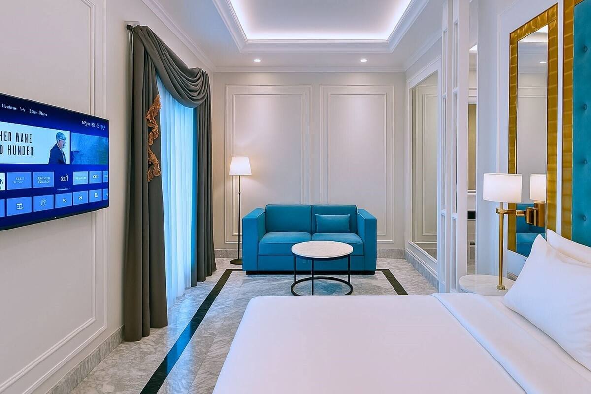 Une chambre d’hôtel avec un lit, un canapé bleu, une petite table ronde et un téléviseur fixé au mur.