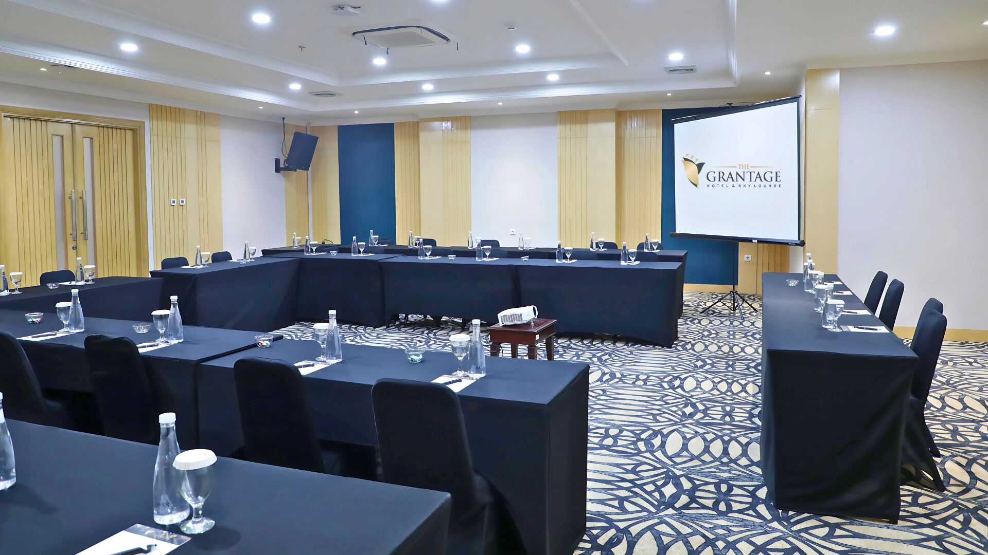 A conference room with a long table, chairs, and a projector screen.