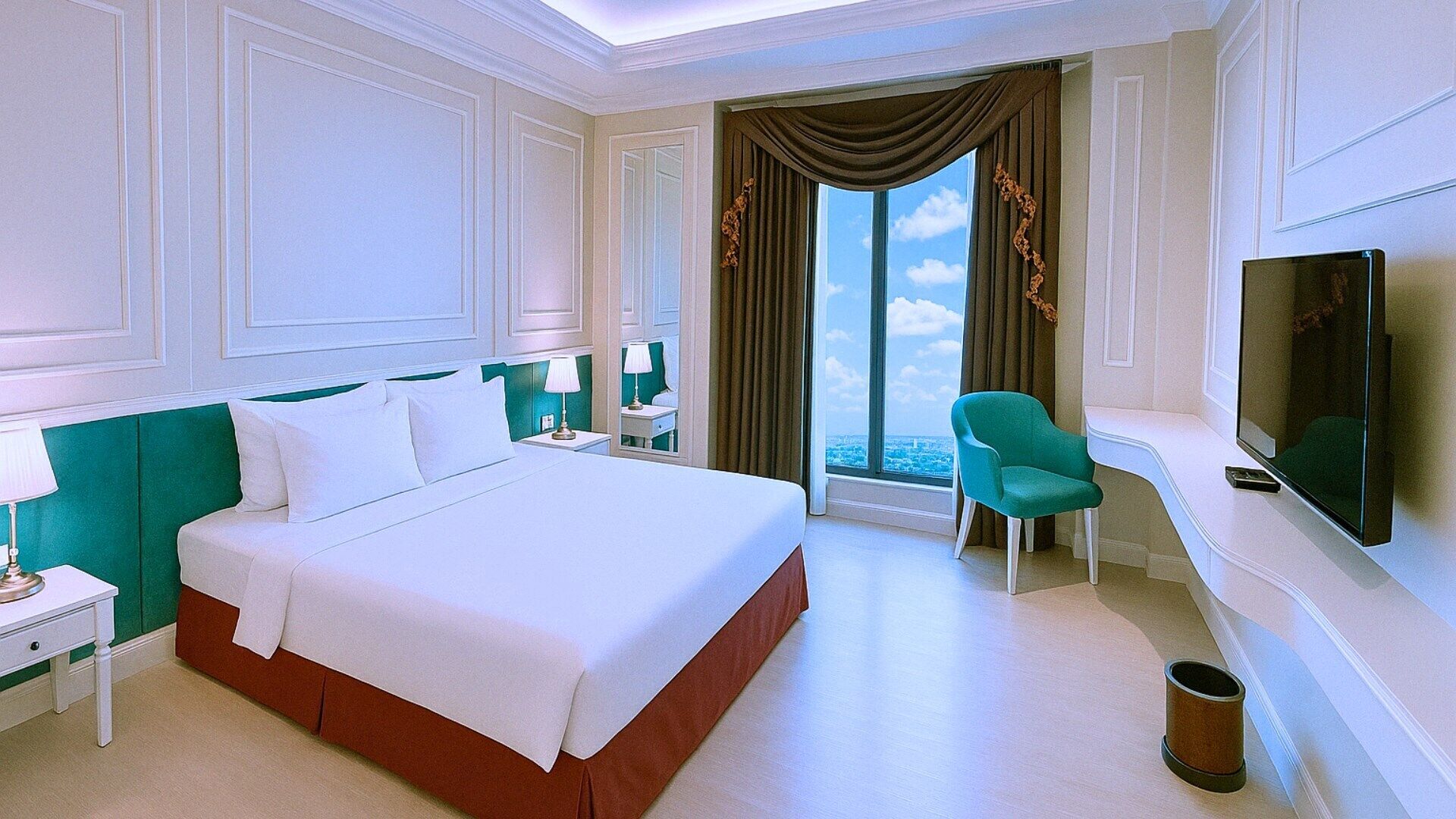 A hotel room with a large bed, a television, a desk, and a view of the city through the window.