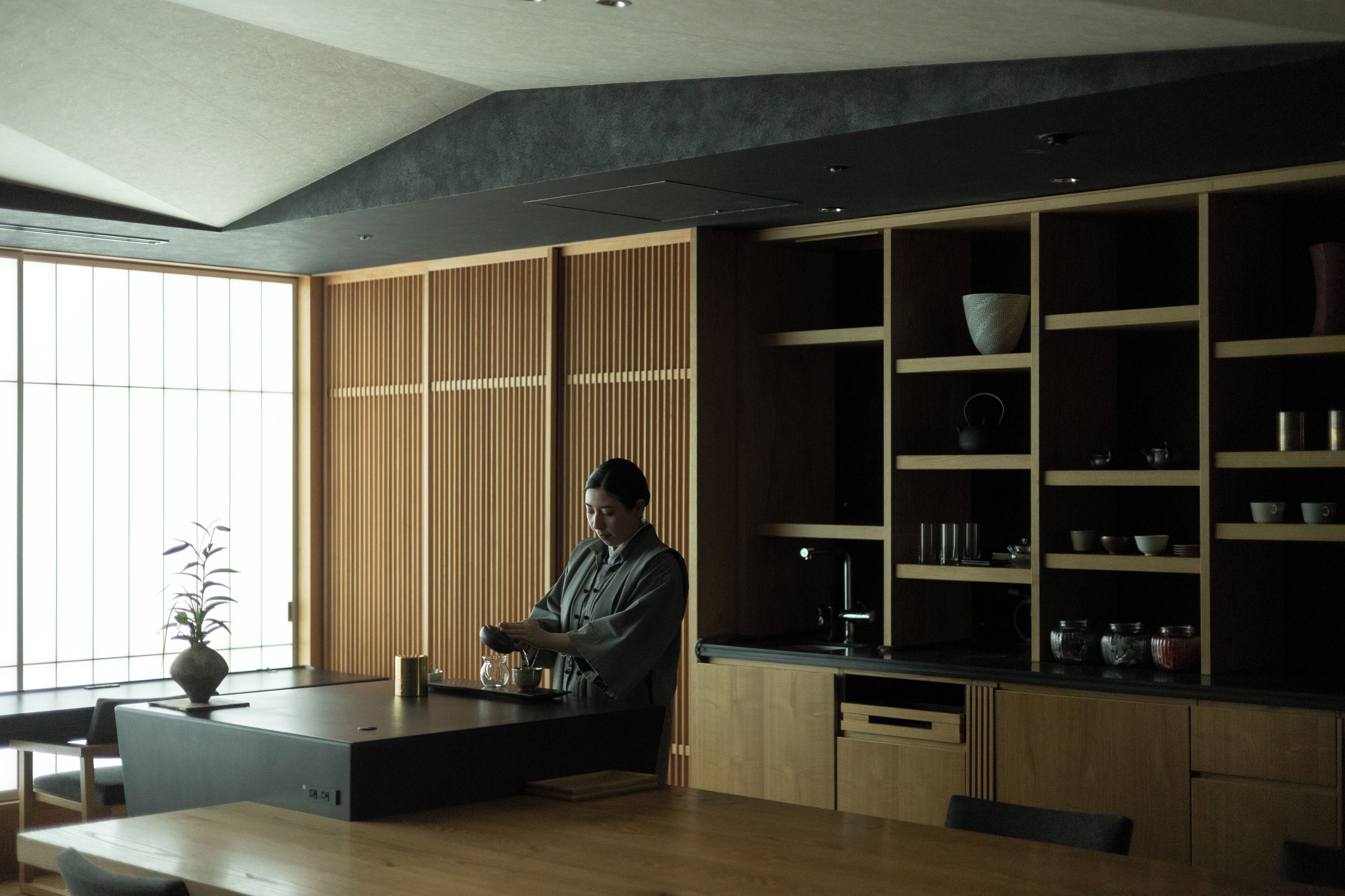 A modern kitchen with a person preparing food, wooden cabinets, and a large window.