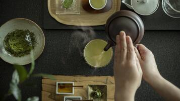 Una persona sirviendo té desde una tetera a una taza, con hojas de té y una tetera sobre una bandeja de madera.