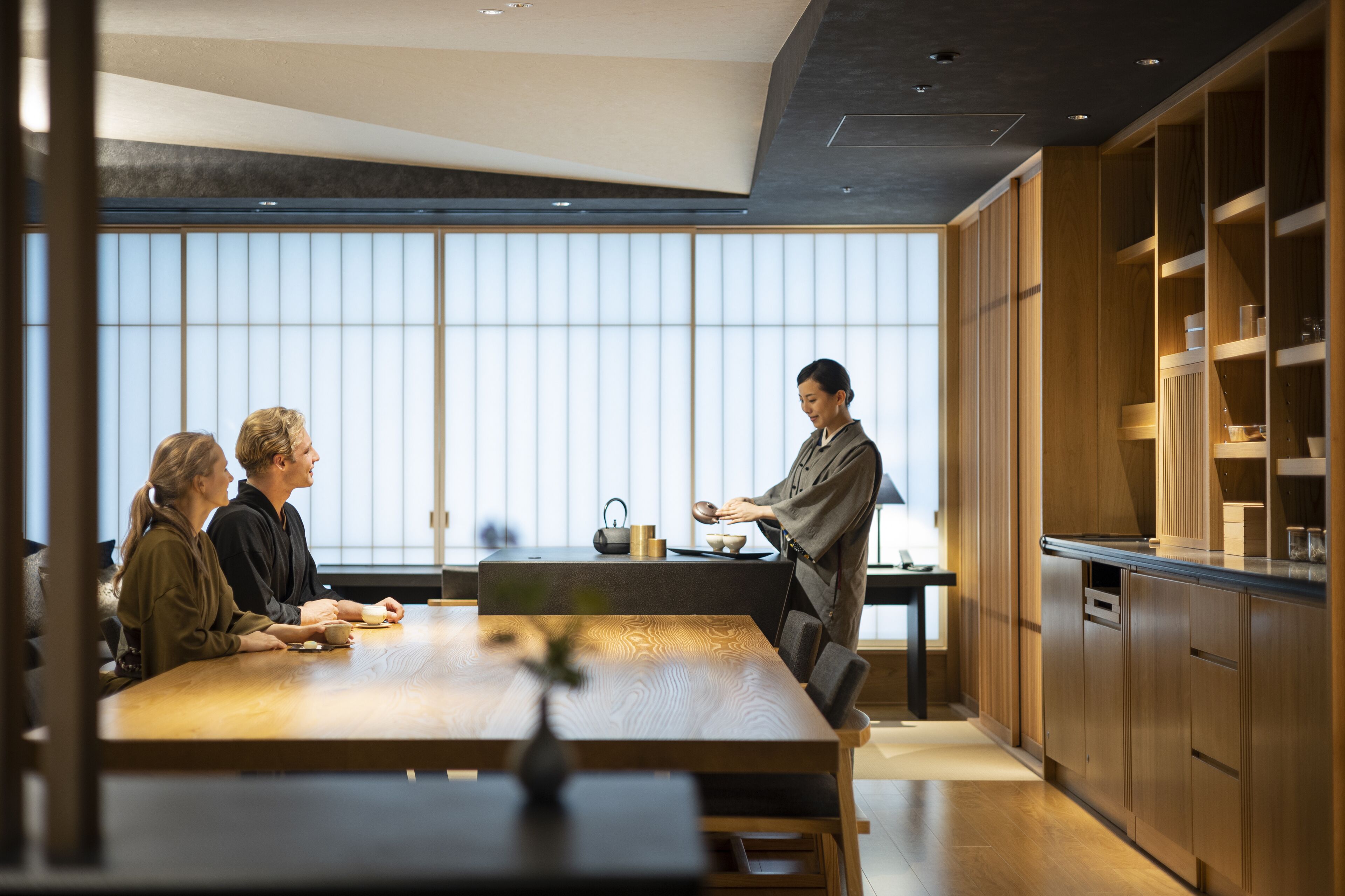 A modern kitchen with wooden cabinets, a large dining table, and a view through the window.
