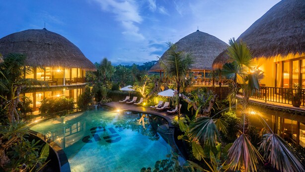 Un resort con piscina, edificios de techo de paja y exuberante vegetación.