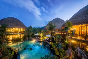 Un resort con piscina, edificios de techo de paja y exuberante vegetación.