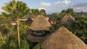 Cabañas con techo de paja y zonas de estar al aire libre, rodeadas de palmeras y un paisaje exuberante.