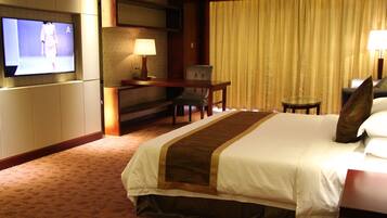 Habitación de hotel con una cama grande, un escritorio con silla, televisor y ventana con cortinas.