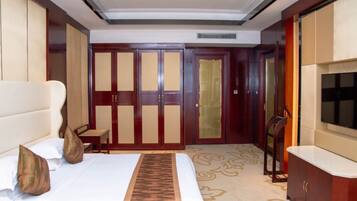 A hotel room with a large bed, a TV, a wardrobe, and a desk.
