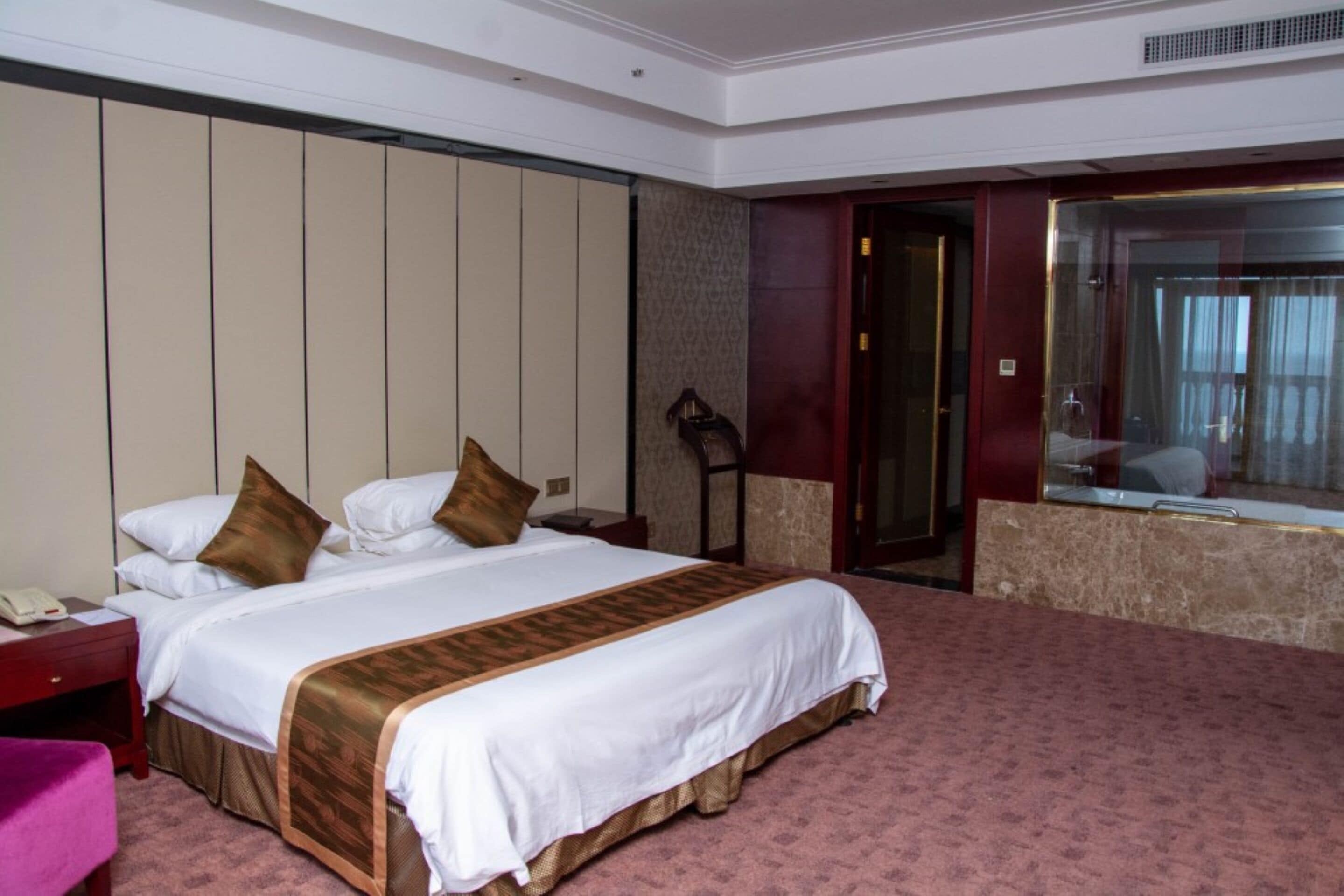 A hotel room with a large bed, a nightstand, a desk, a chair, a mirror, and a door.