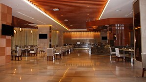 Un amplio hall de hotel con piso pulido, techo de madera y zona de bar central.