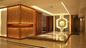 A lobby with a wooden reception desk, a central illuminated display, and a marble floor.