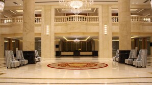 Un amplio vestíbulo con suelo de mármol, un candelabro central y un diseño de alfombra circular.