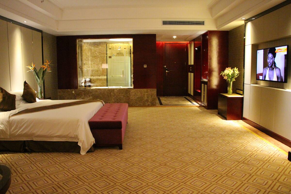 Une chambre d’hôtel dotée d’un grand lit, d’un coin salon, d’une télévision et d’une salle de bain avec une paroi en verre.