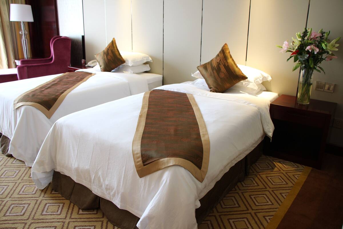 Une chambre d’hôtel avec deux lits, chacun agrémenté d’un couvre-lit marron, de draps blancs et d’un vase de fleurs placé sur la table de chevet.