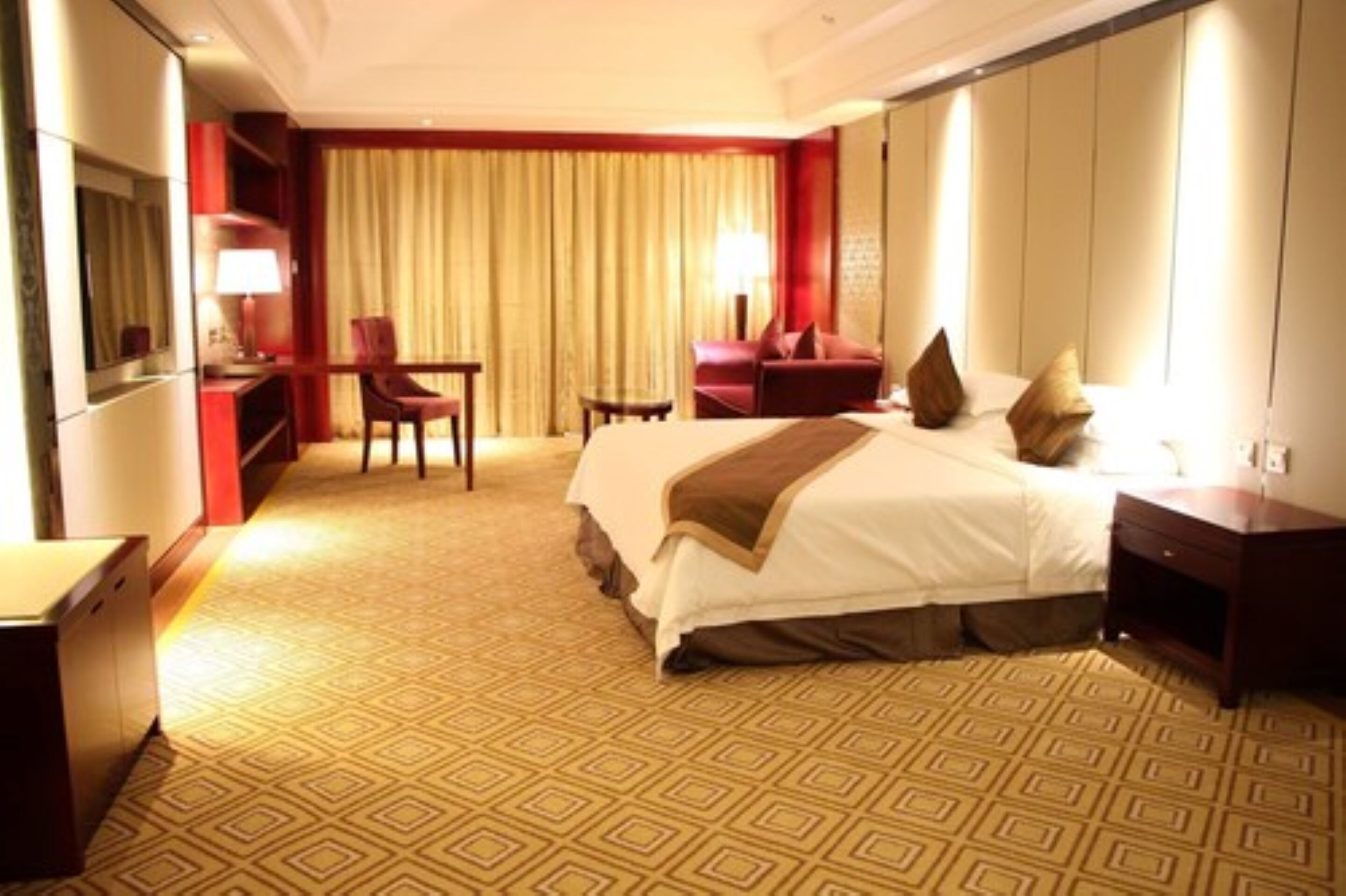 A hotel room with a large bed, a desk, a chair, and a TV.