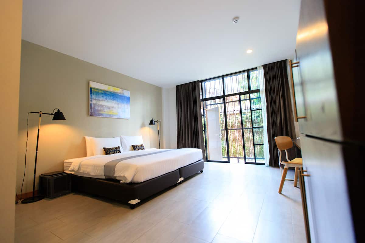 A modern bedroom with a large bed, a desk, and a chair. There is a window with curtains and a painting on the wall.