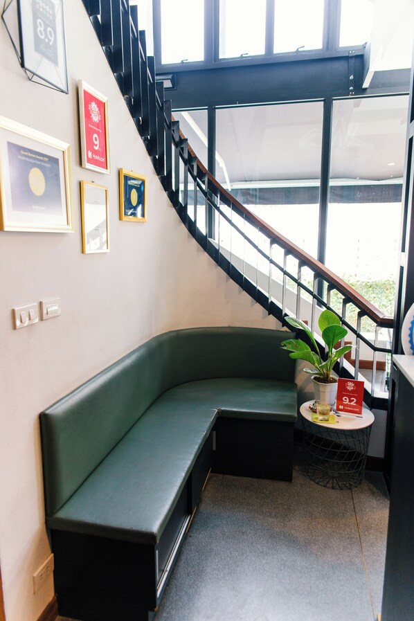 A corner seating area with a green bench, a small round table with a potted plant, and a staircase with a black railing. - Wealth Boutique Hotel (Chiang Mai)