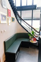 A corner seating area with a green bench, a small round table with a potted plant, and a staircase with a black railing.