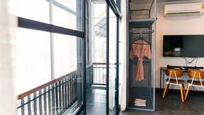 Ein modernes Hotelzimmer mit großen Fenstern, einem Balkon, einer Sitzecke mit Fernseher und einem Kleiderständer.