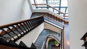 Eine moderne Treppe mit hölzernem Geländer und schwarzen Metallspindeln, die in ein unteres Geschoss führt.
