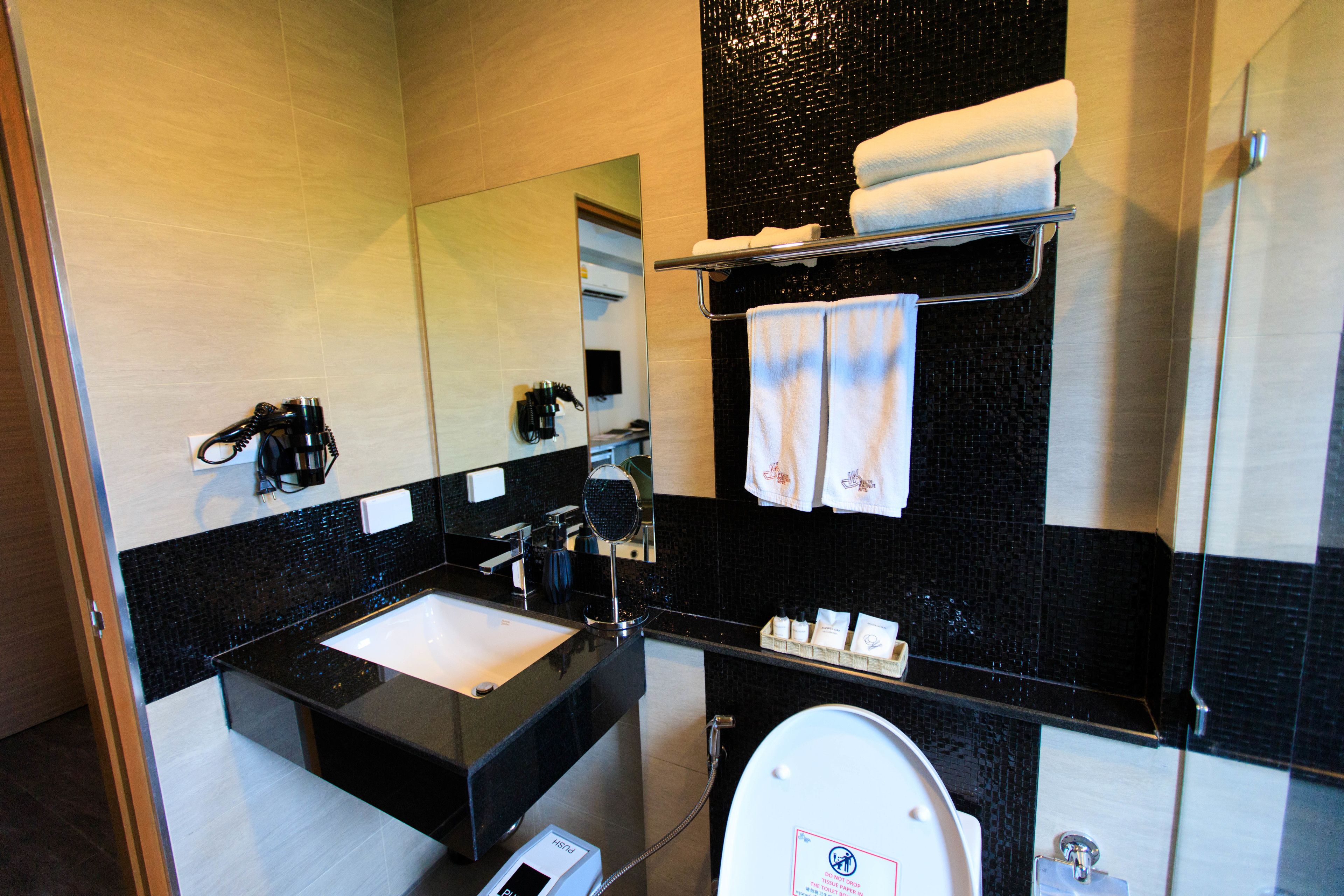 A modern bathroom with a black and white tiled wall, a sink, a toilet, and a mirror.