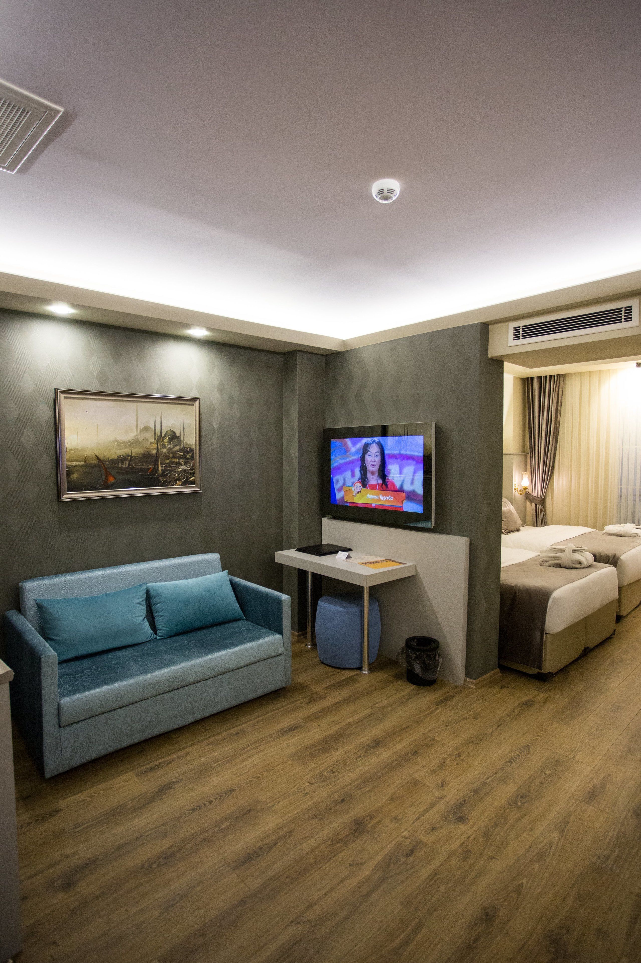 A modern hotel room with a TV, a sofa, a small table, and a bed.