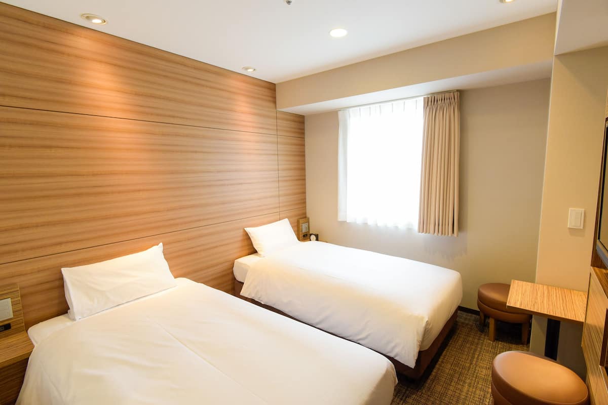 Quarto de hotel com duas camas, uma pequena área de estar, uma janela com cortinas e uma parede de madeira.