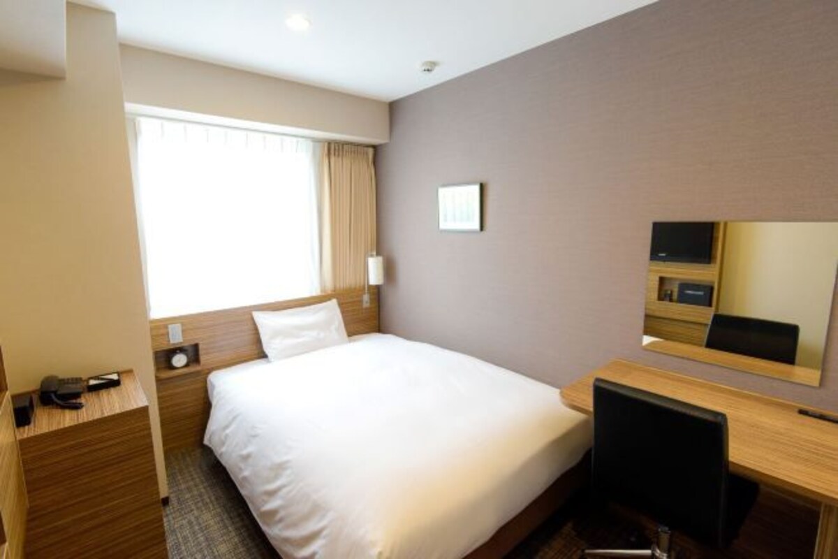 A hotel room with a bed, a desk, a chair, a TV, and a window with curtains.