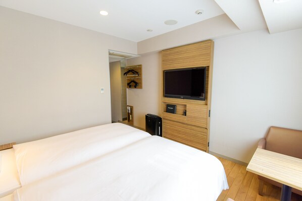 Habitación de hotel con una cama grande, un televisor montado en la pared, una mesita pequeña y un perchero con perchas.