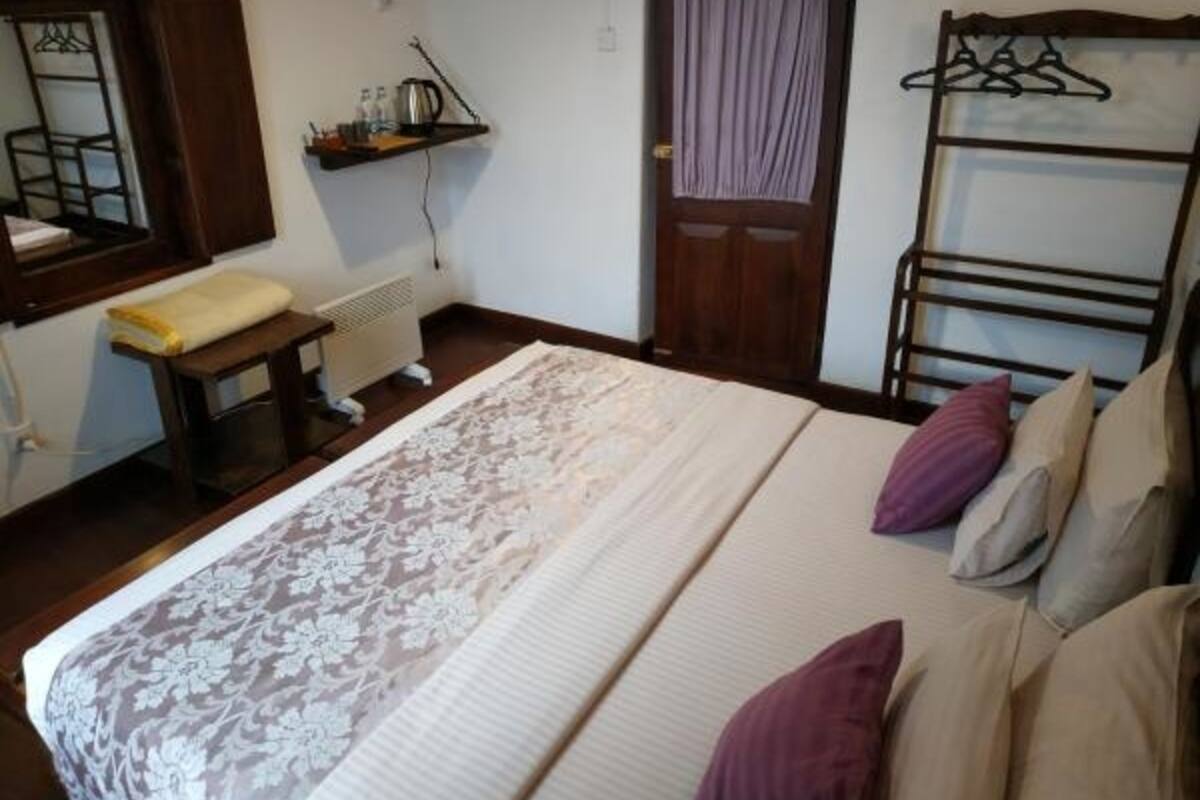 A bedroom with a bed, a bedside table, a radiator, a door with a curtain, and a coat rack.