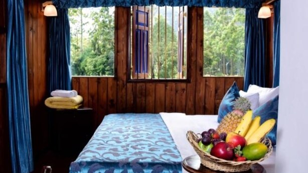 Une pièce de cabane en bois comprenant un lit, un panier de fruits et une fenêtre avec des rideaux.