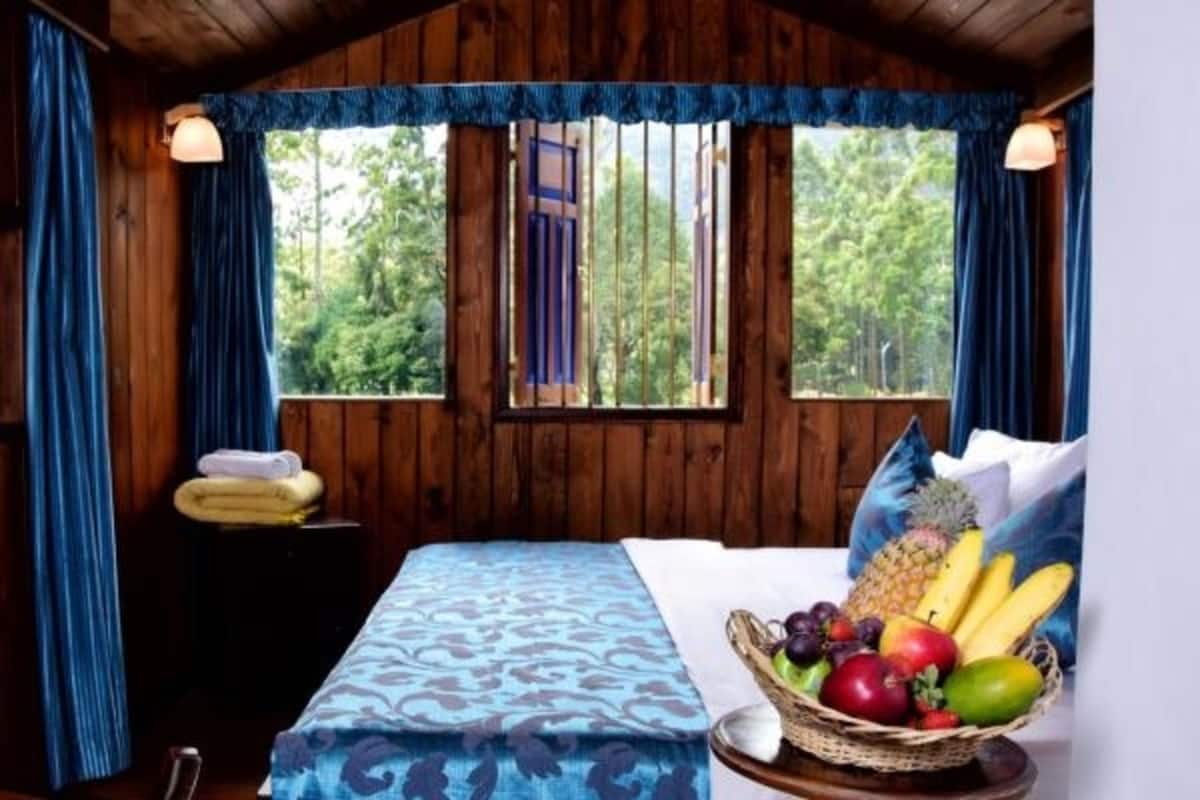 A wooden cabin room with a bed, a basket of fruit, and a window with curtains.
