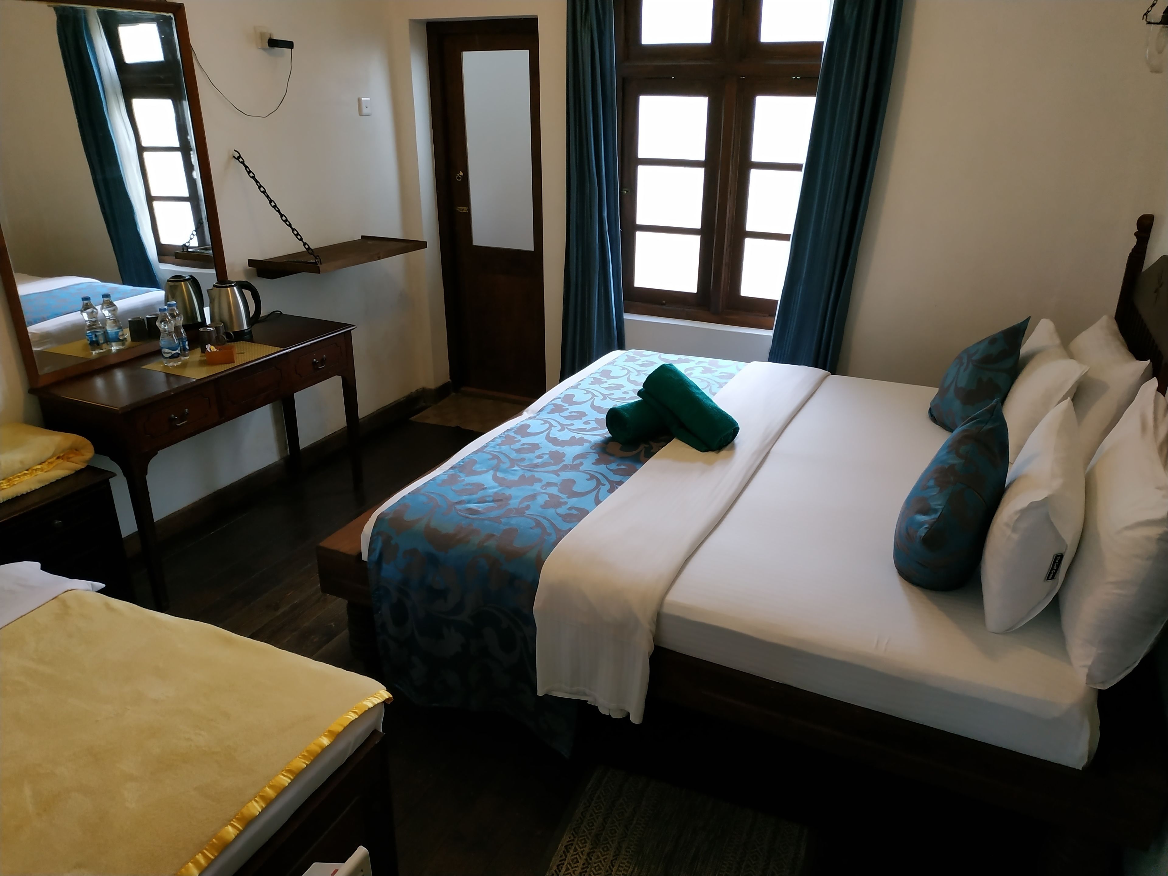 A hotel room with a bed, a desk, a mirror, and a window with curtains.