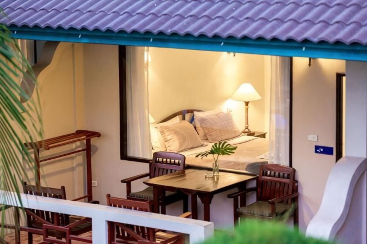 A room with a bed, a desk, and a chair, with a view of a balcony.