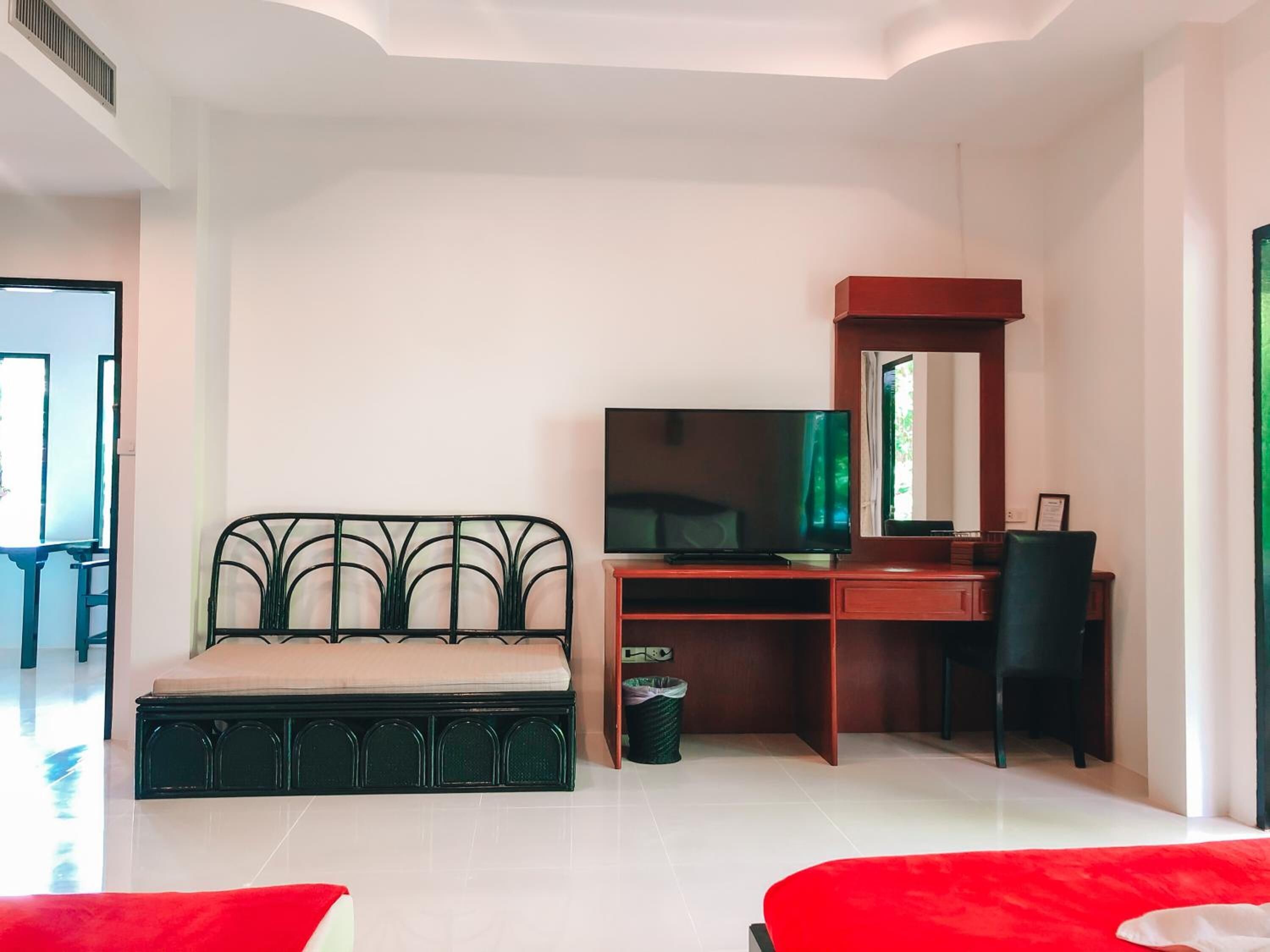 Un dormitorio moderno con cama, escritorio con televisor, silla y sofá rojo.