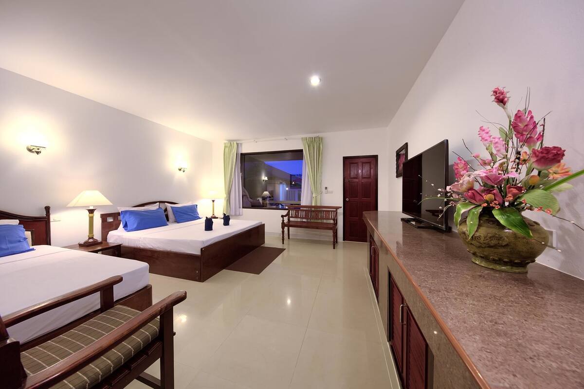 Una habitación de hotel con cama, escritorio, silla, televisor y un jarrón de flores.