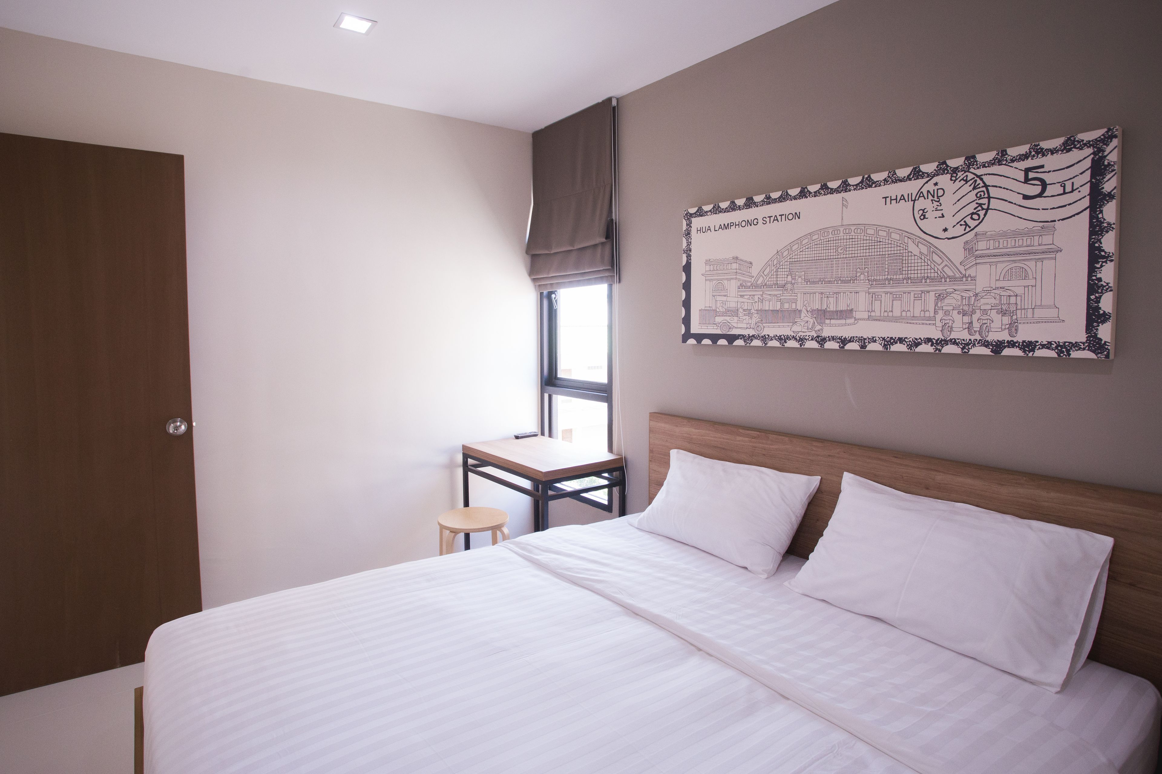 A hotel room with a bed, a small table, a window with a view, and a wall with a framed picture.