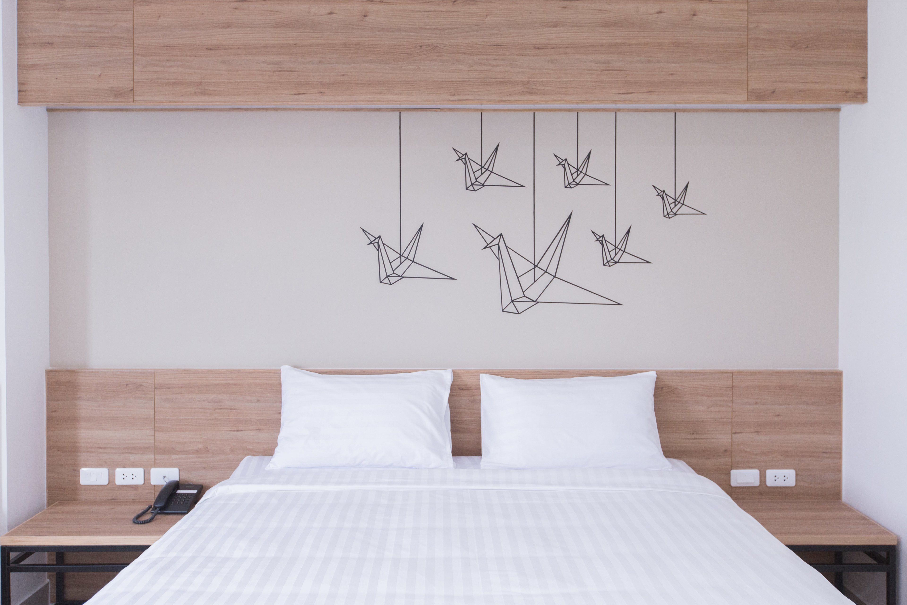 Une chambre d’hôtel comprenant un lit, deux tables de chevet, une tête de lit en bois et une œuvre d’art fixée au mur, composée de formes géométriques.