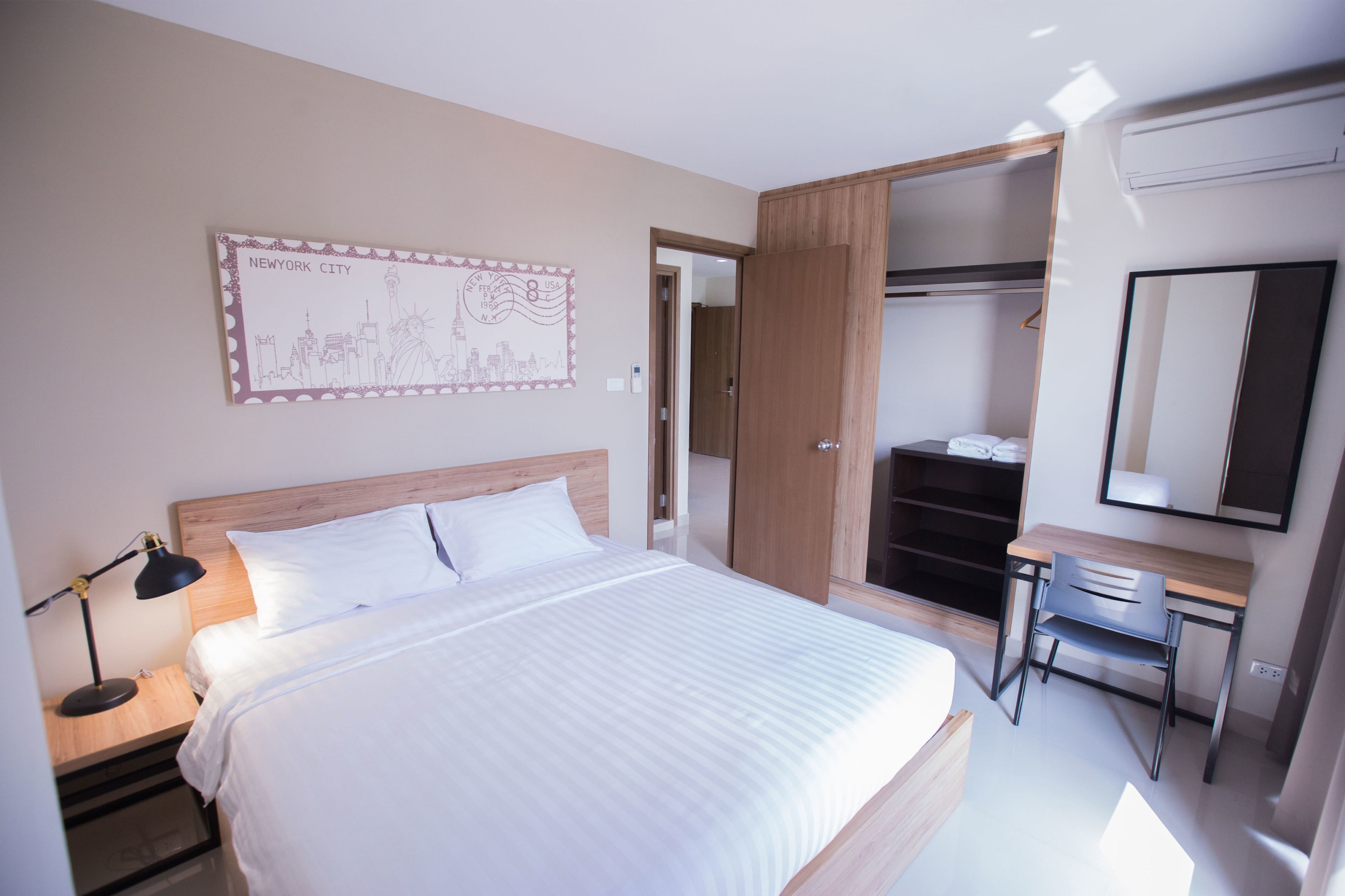 A hotel room with a bed, a desk, a mirror, a wardrobe, and a wall-mounted artwork of New York City.