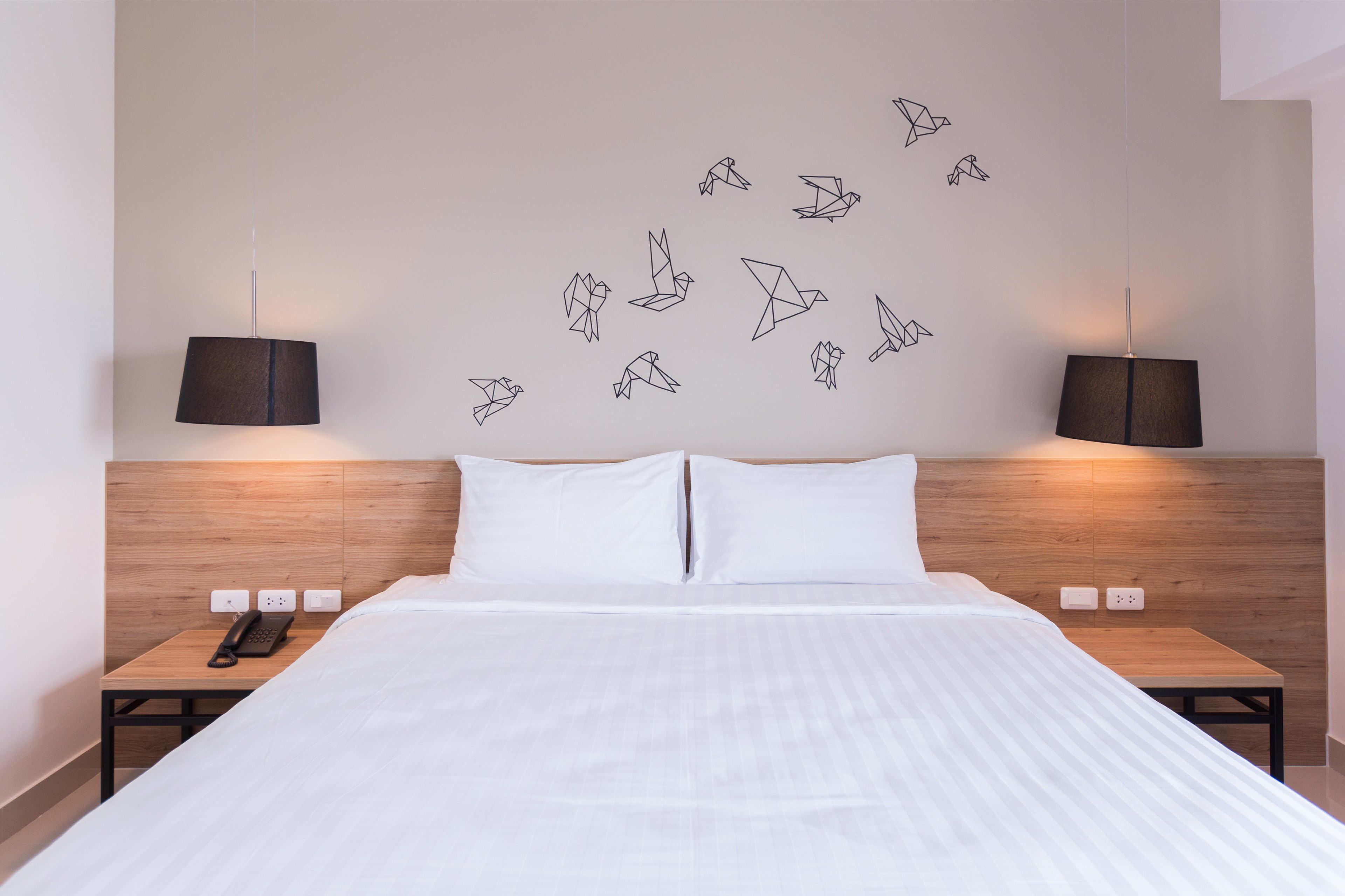 Habitación de hotel con una cama grande, dos mesitas de noche con lámparas y una pared decorada con pájaros de origami.