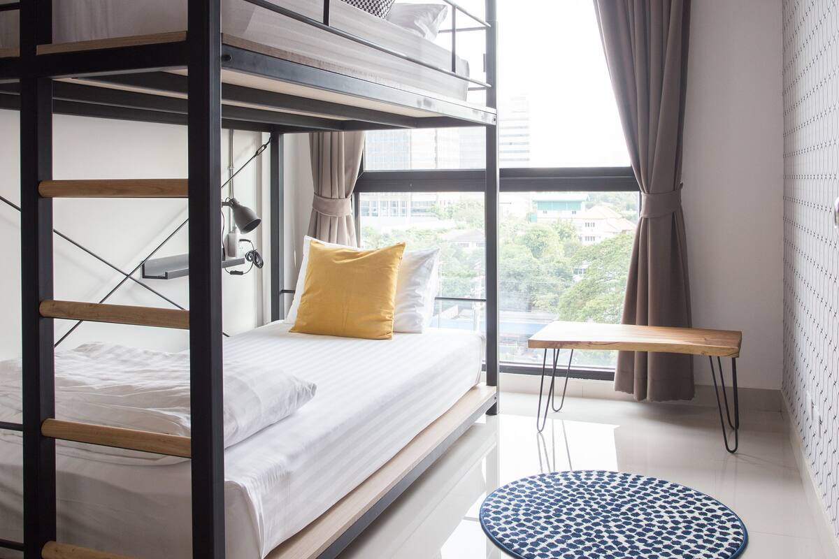 Habitación con literas, una ventana, un escritorio y una alfombra redonda.