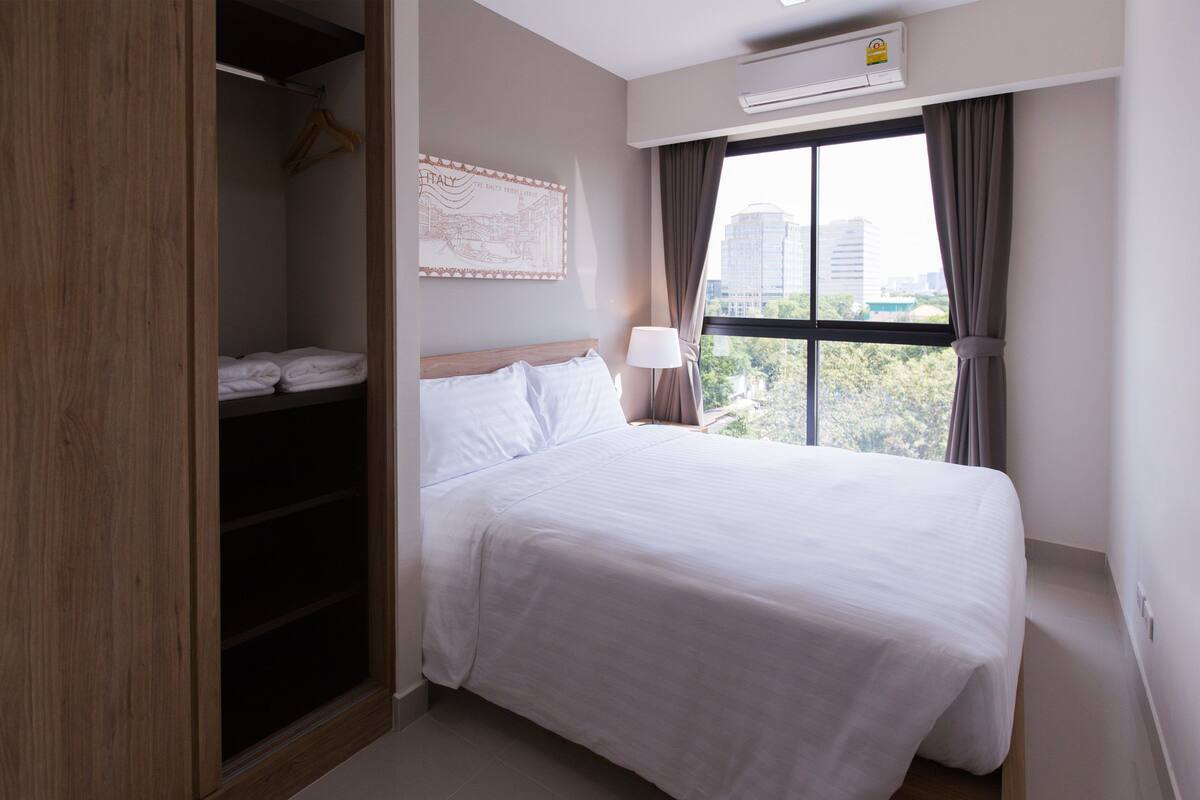 Una habitación de hotel con cama, armario, ventana con cortinas y aire acondicionado instalado en la pared.